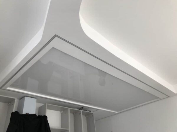 Lesklý napínaný strop nad kuchyňským ostrůvkem v bílé barvě a skříňkami