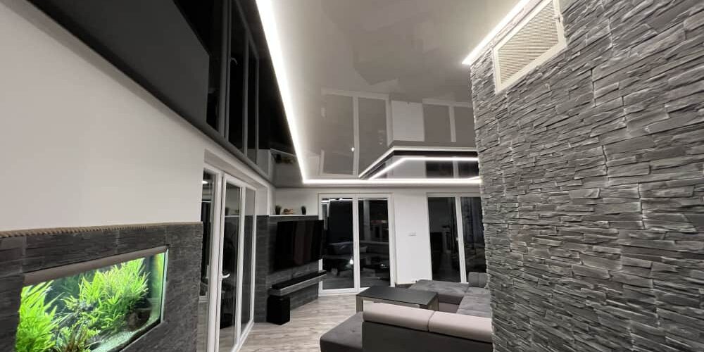 Jednobarevný lesklý napínaný strop s LED podsvícením Černý lesklý napínaný strop s minimalistickým LED osvětlením v moderním obývacím pokoji Designový prvek, který opticky zvětšuje prostor a dodává interiéru hloubku