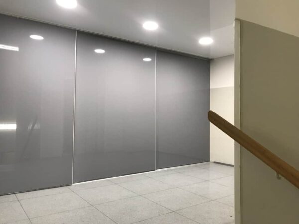 Moderní chodba s lesklou šedou napínanou fólií na posuvných stěnách  Reflexní povrch opticky zvětšuje prostor a zajišťuje elegantní vzhled s praktickým využitím 