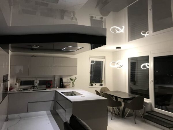 Moderní kuchyně s lesklým napínaným stropem, který odráží LED osvětlení a interiérový design  Jídelní kout s elegantním stolem a židlemi ladí s minimalistickou kuchyňskou linkou a ostrůvkem 