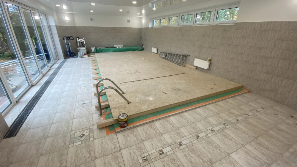 Bazén v interiéru zakrytý OSB deskami pro bezpečný pohyb montážního lešení při instalaci napínaného stropu